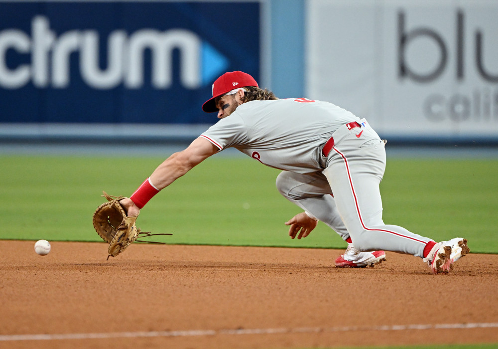 Bryce Harper makes a dive for a ground ball at first base. The ball is about to reach his outstretched glove, which is on his left hand.