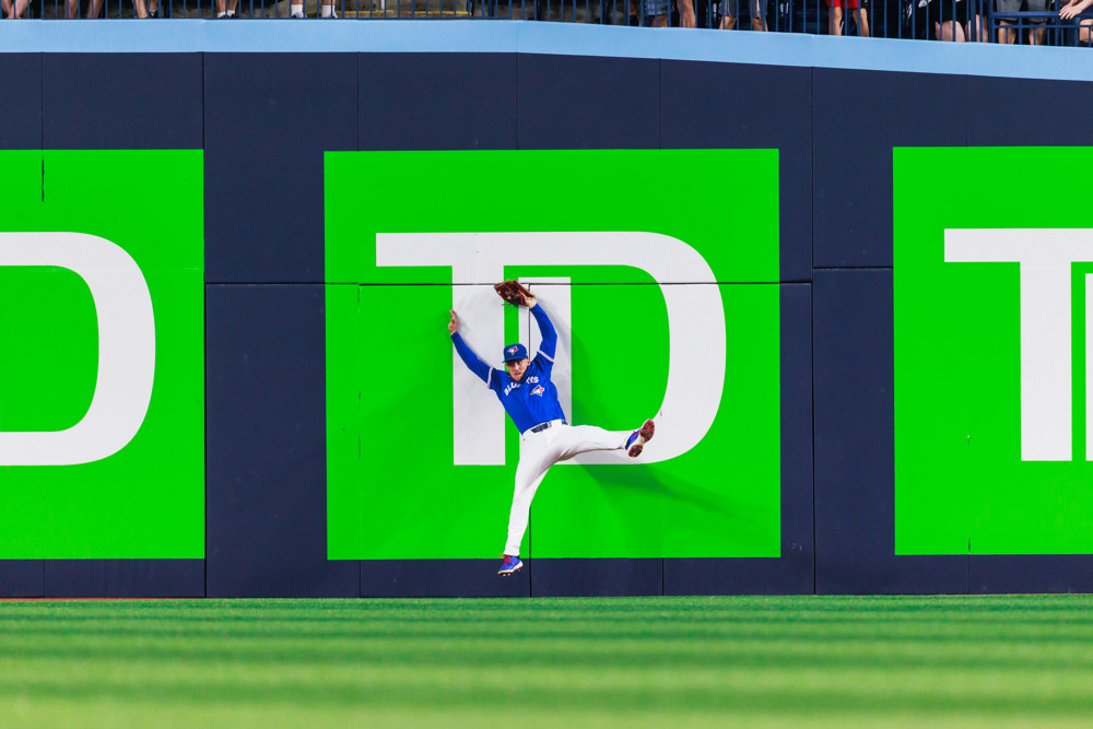 Myles Straw, arms raised, bounces off the center field fence to make a catch.