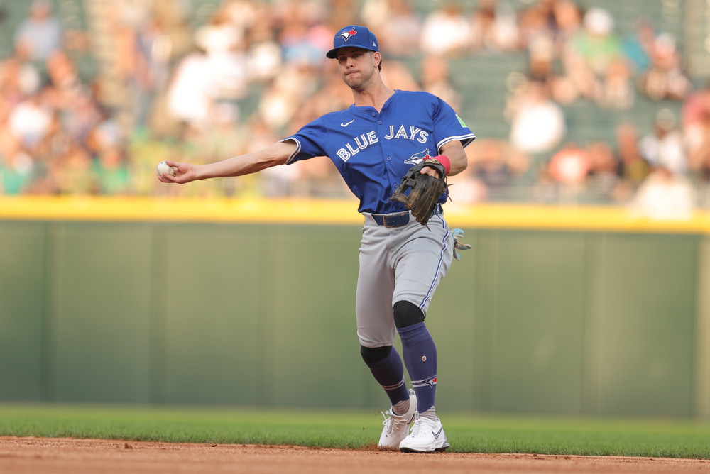 Ernie Clement makes a sidearm throw to first base. He's wearing a blue Jersey and grey pants.