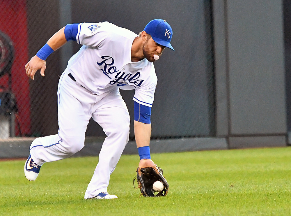 Kansas City Royals' leftfielder Alex Gordon (4- white jersey, blue lettering) fields a ball with the glove on his left hand is he leans forward to pick it up.