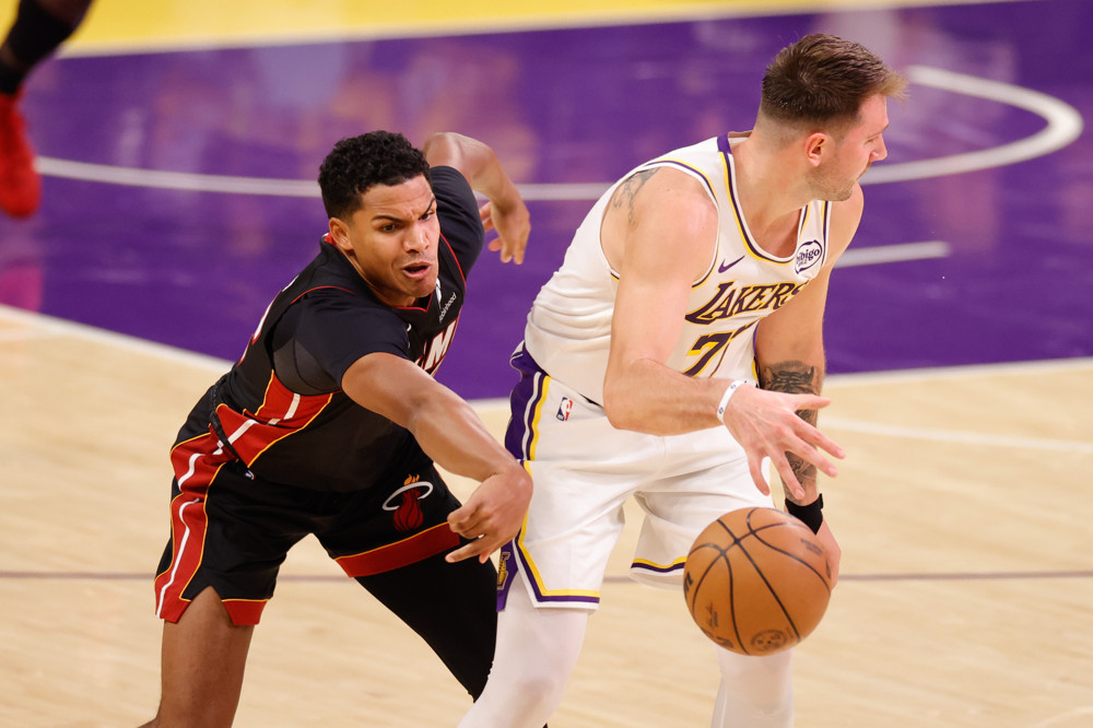 Dru Smith, in a black Miami heat jersey and black shorts, reaches with his right hand to poke the ball away from a player in a white Lakers jersey who is protecting the dribble with his right hand.