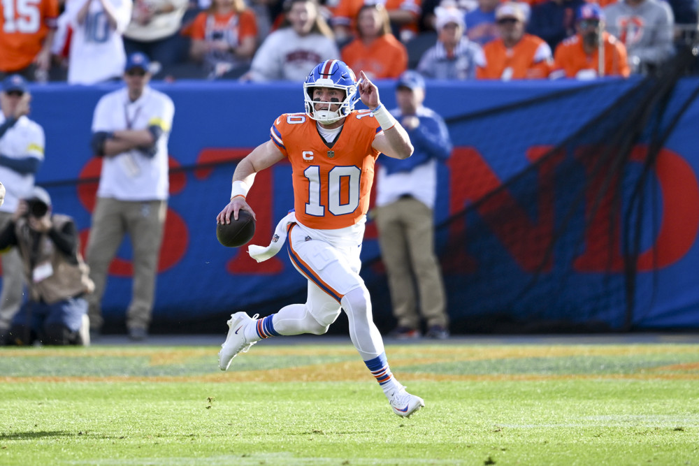 Bo Nix, wearing an orange jersey with a white #10 and white pants, runs up the field while pointing with his left hand and index finger.