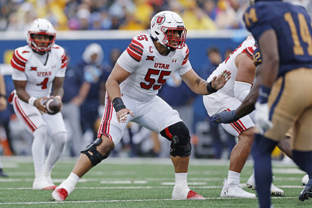 Spencer Fano, wearing a white #55 Utah football jersey crouches slightly, ready to block anyone in his path.