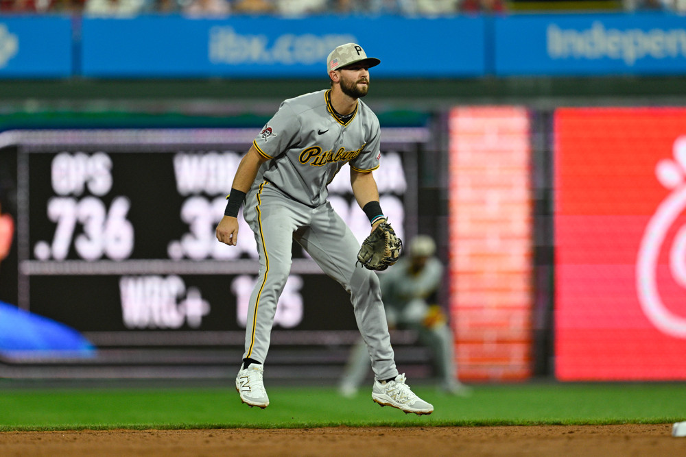 Jared Triolo, wearing a grey Pirates baseball jersey, grey pants, and a grey baseball cap, stands in a ready position waiting for a ball to be hit to him.