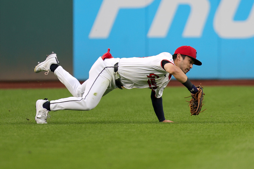 Steven Kwan, wearing a white Guardians jersey and white pants, dives to his right with a full extension to catch a ball.