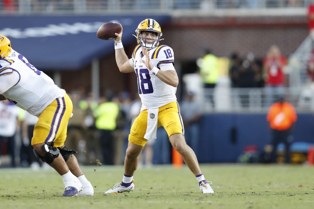 Garrett Nussmeier, a LSU quarterback wearing yellow pants, a white jersey and yellow helmet, raises his right arm with football in hand, preparing to throw a pass.