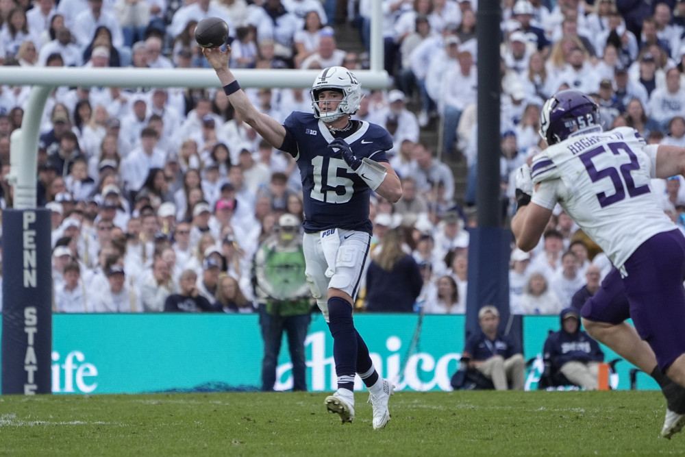 Drew Allar, wearing a blue Penn State jersey, white pants and a white helmet, releases a pass to his right with his right hand.