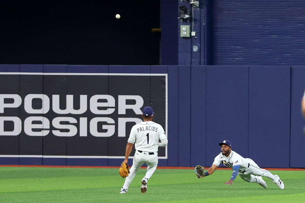 Cedric Mullins, in white jersey and blue Tampa Bay Rays cap, dives with his glove extended to try to make a catch of a shallow fly ball.