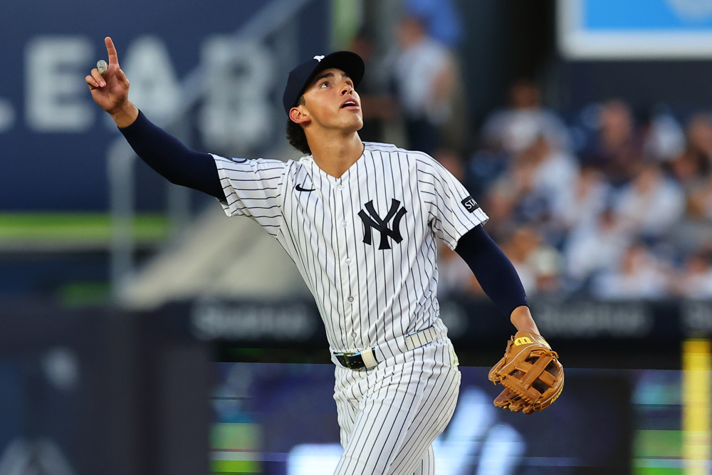 Yankees shortstop George Lombard, wearing a Yankees pinstriped jersey and dark blue cap, waves in the air with his right hand to indicate he's going to make a catch.