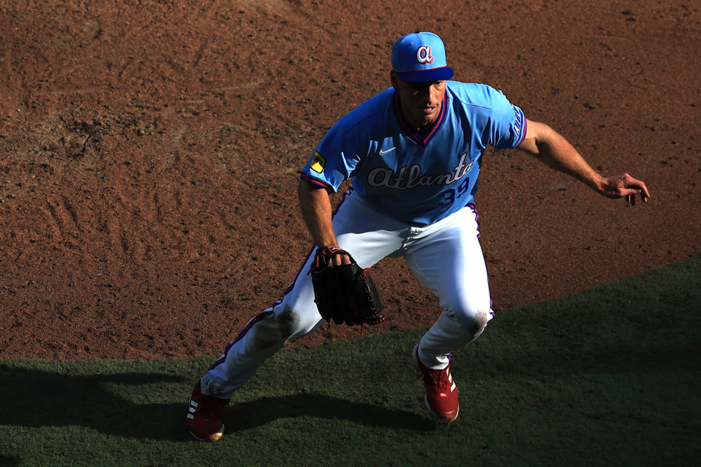 Brent Suter, wearing a light blue Braves jersey and cap, comes forward to field a ball.